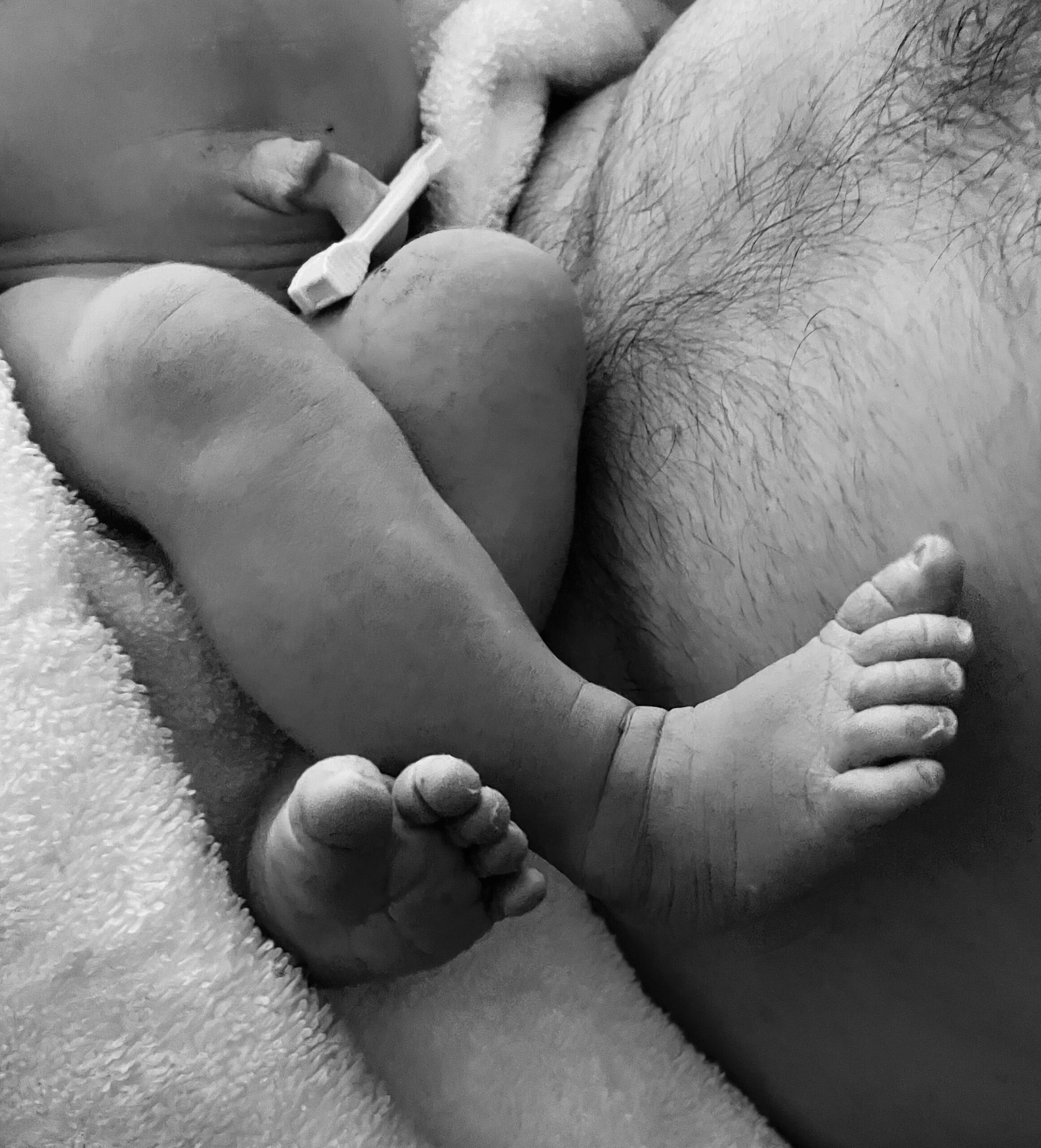 Black and white photo of a baby resting on an adult's chest.