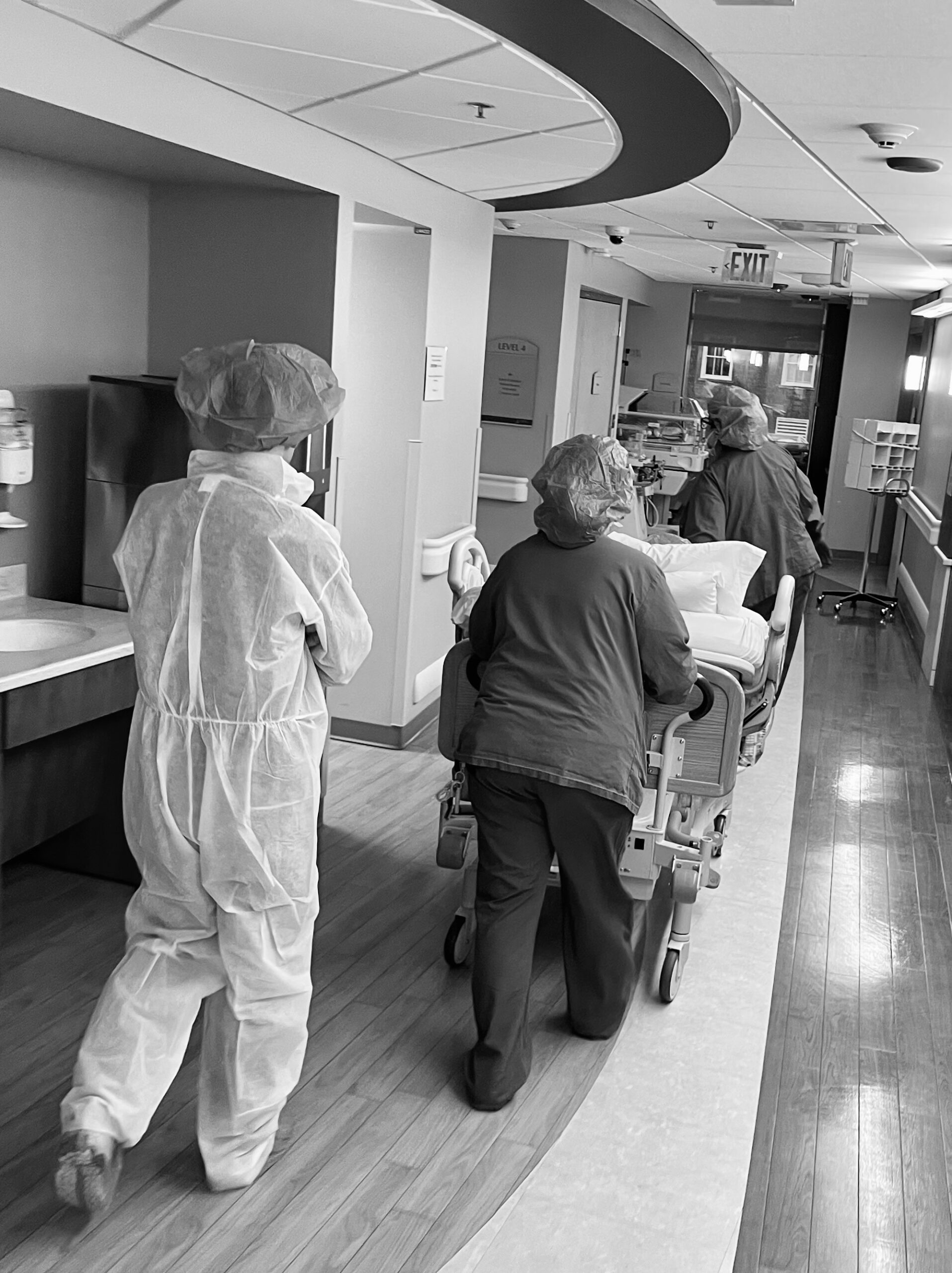Healthcare workers assisting a patient on a hospital bed in a hallway.