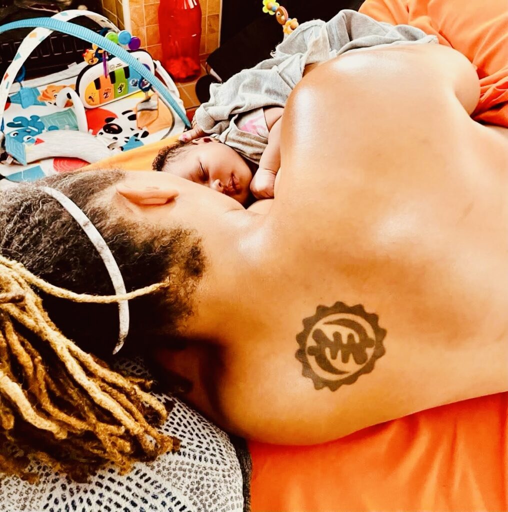 A person with dreadlocks and a tattoo on their shoulder resting on an orange surface.