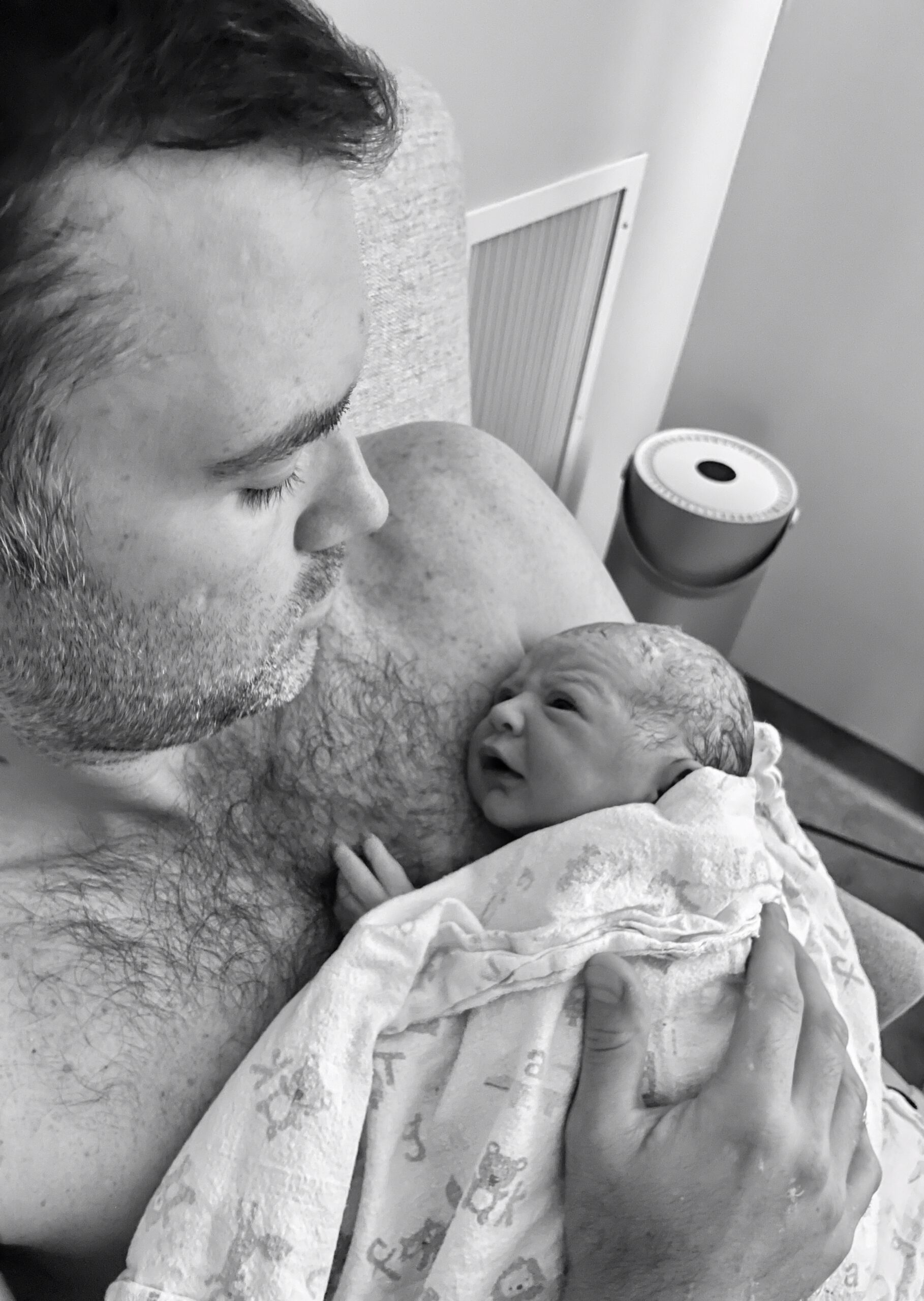 Father tenderly holds newborn baby wrapped in a blanket.