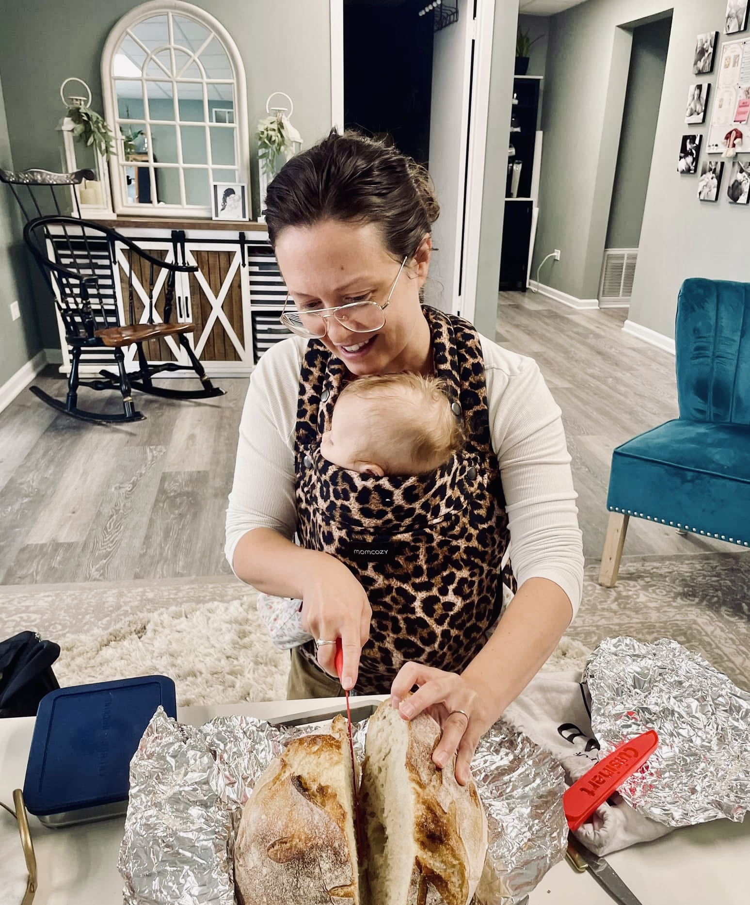 Woman preparing food while carrying a baby in a leopard print carrier.