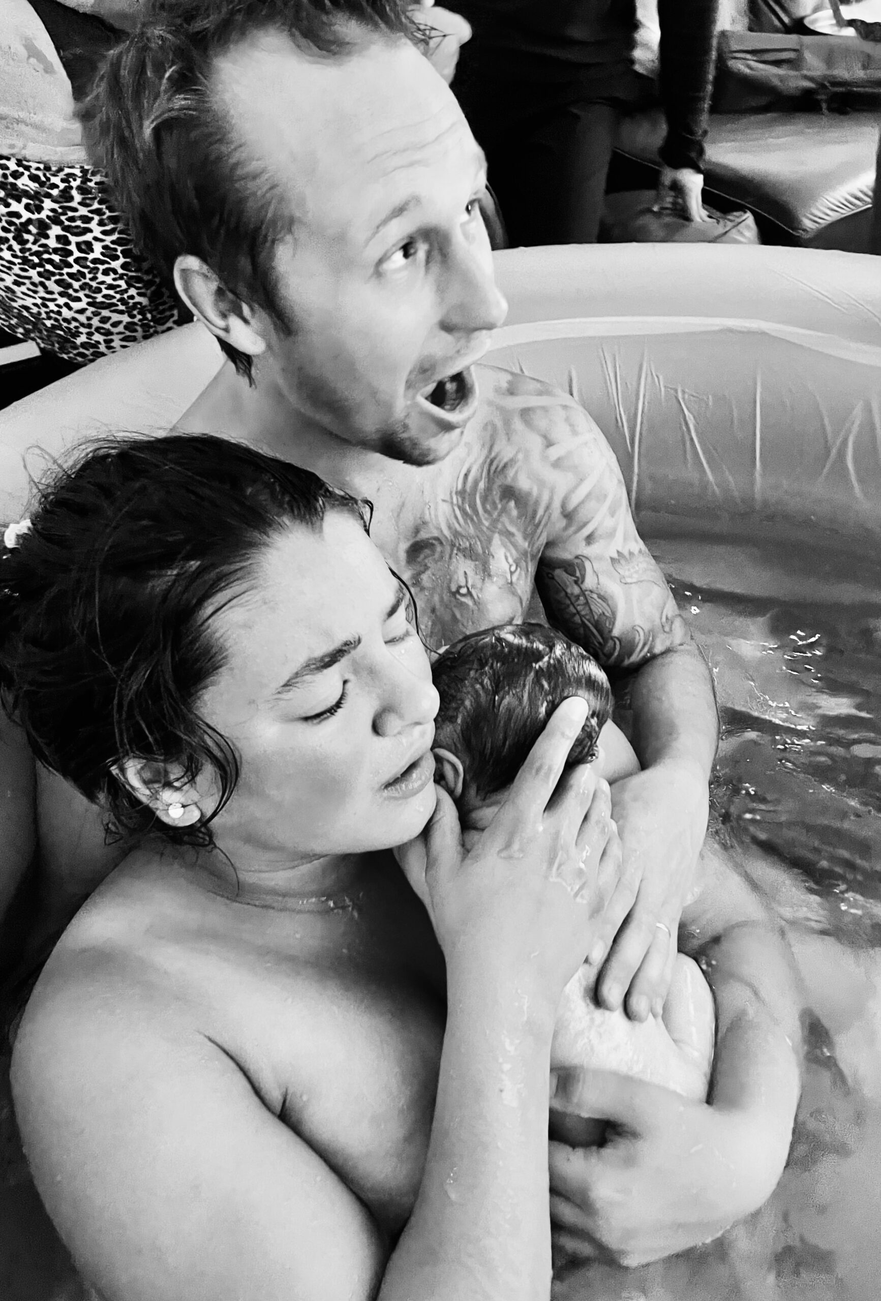 Parents embrace their newborn in a birthing pool.