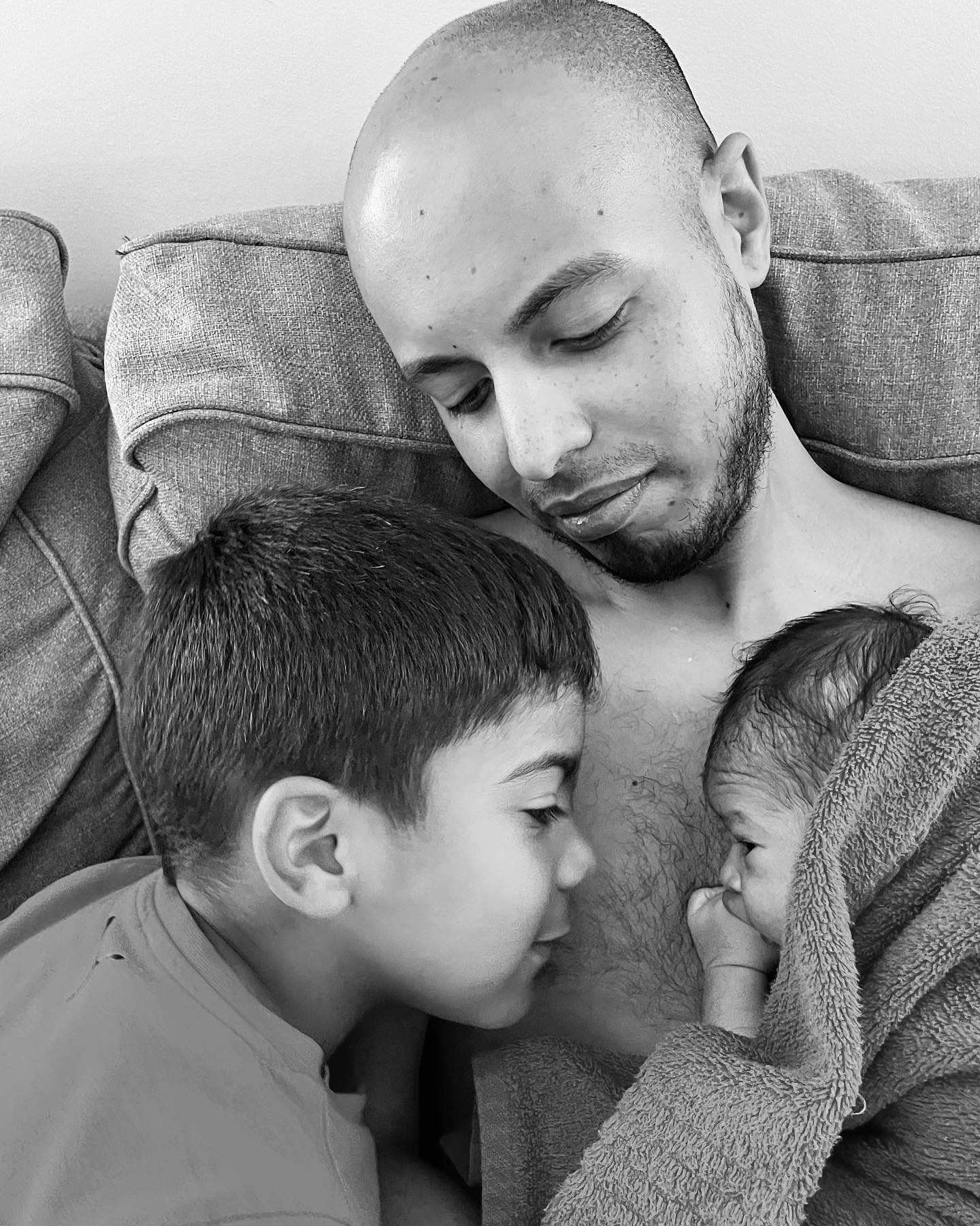 A tender moment of a father cuddling with his two children on a couch.