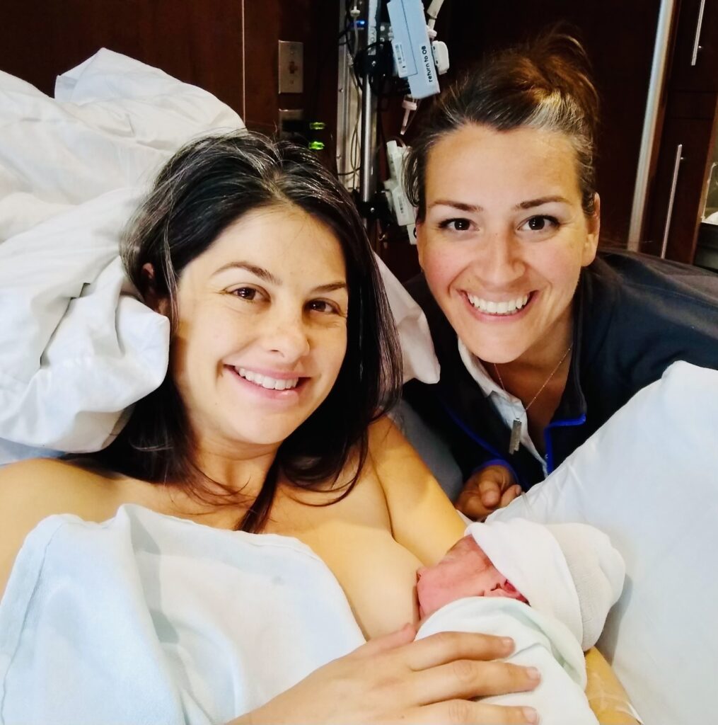 Two women smiling, with one holding a newborn baby.