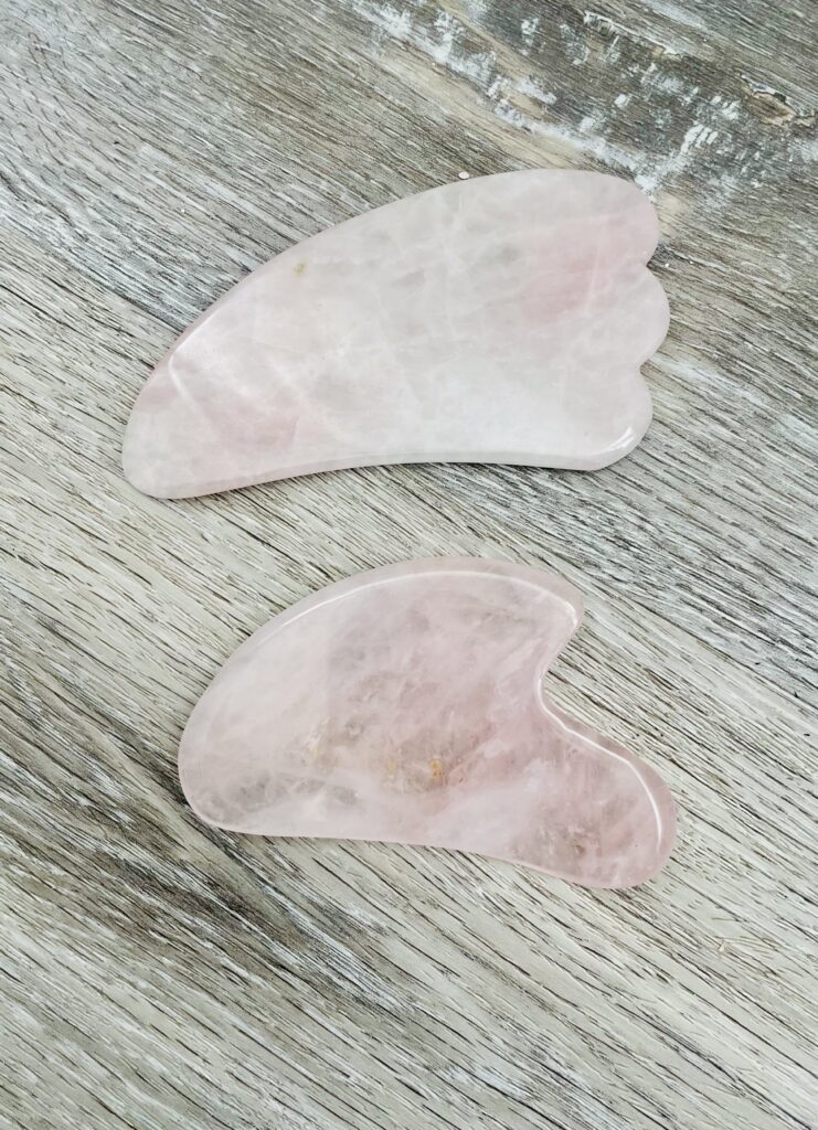 Two rose quartz gua sha stones on a wooden surface.