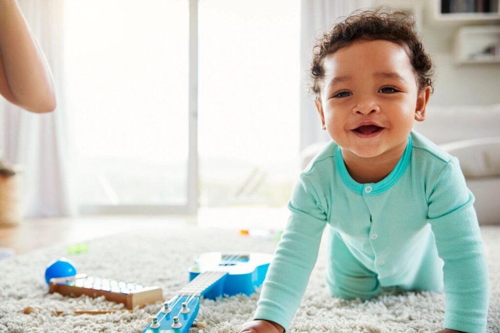 Happy baby crawling on carpet near toys in bright room.