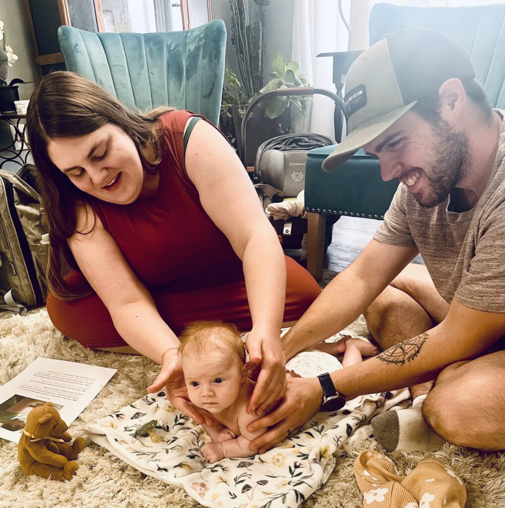 Parents giving a baby a bath at home with toys around.