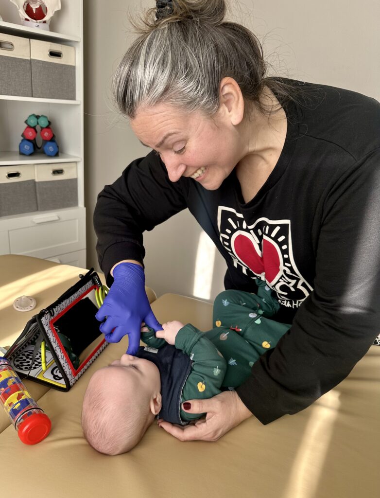 A woman wearing gloves feeds a baby with a syringe.
